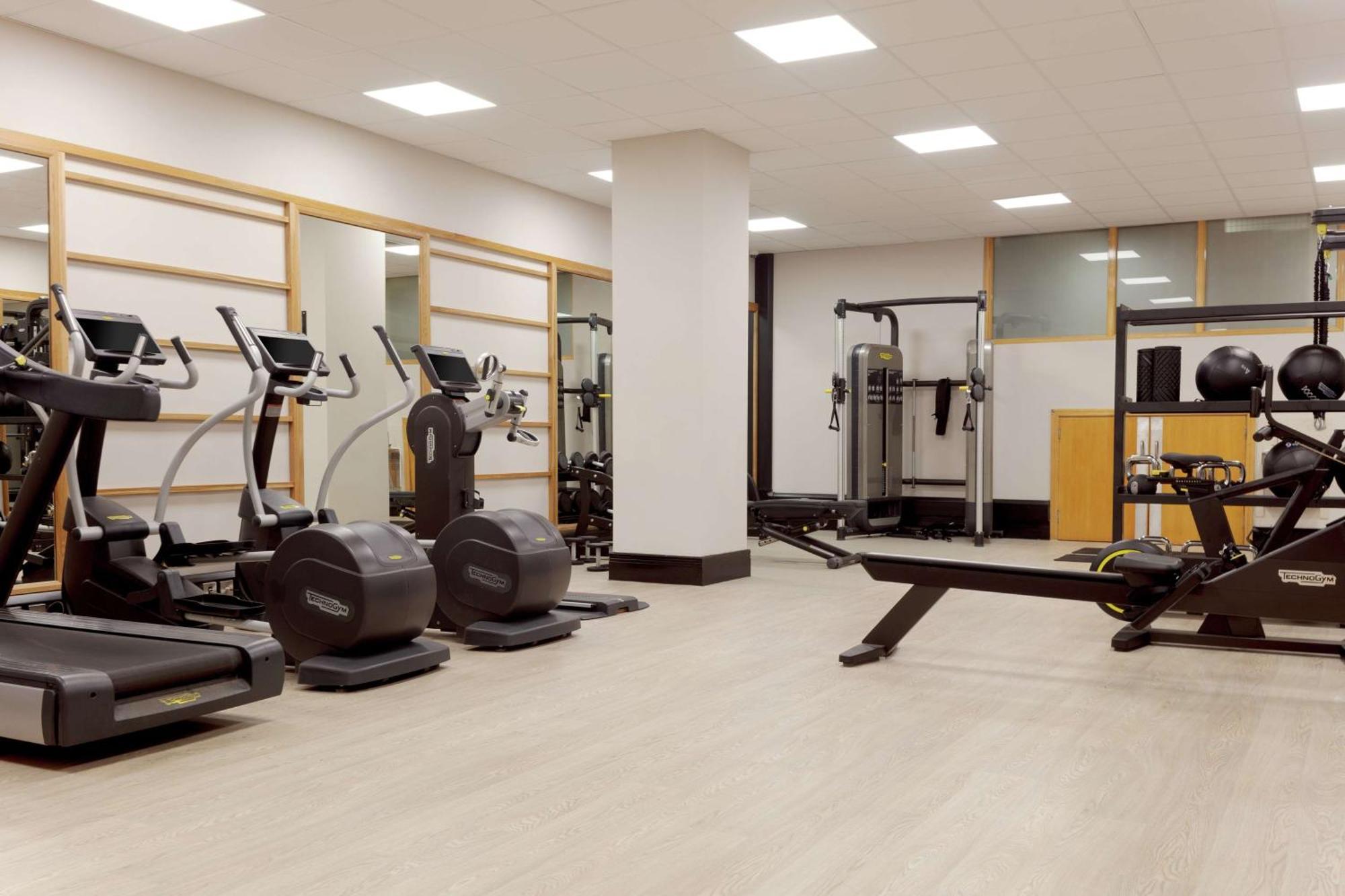 Hilton Belfast Hotel Gym photo The photo shows a gym or fitness area. It features several exercise machines, including treadmills and elliptical machines. There's also a rowing machine and a multi-station strength training equipment. The space is well-lit with overhead lights and 